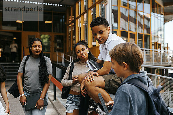 Male and female students discussing while standing at balcony of junior high school