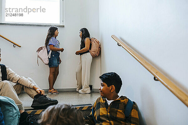 Female friends talking with each other near wall in school