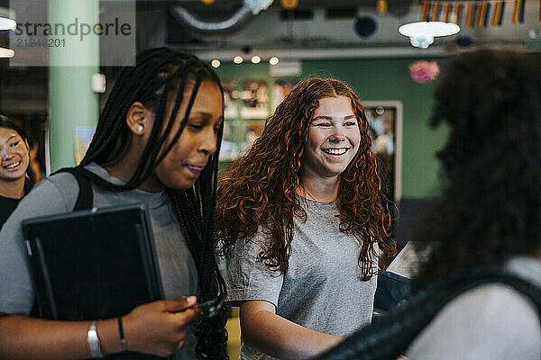 Happy curly haired teenage girl talking with female friends in cafeteria at school