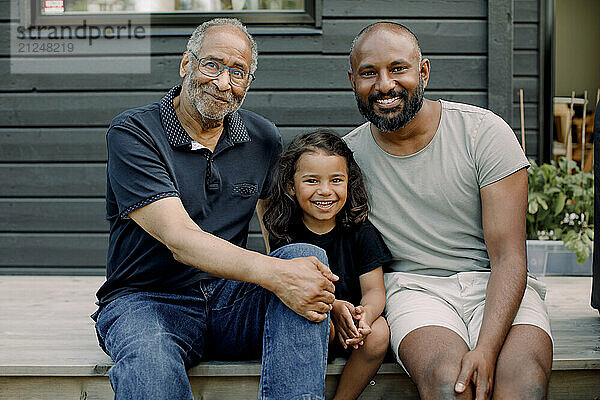 Portrait of smiling boy sitting with father and grandfather on porch