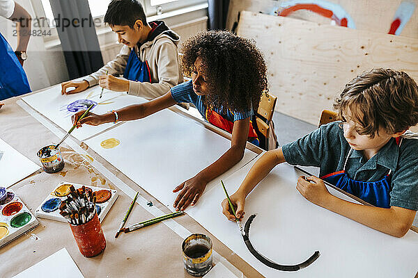 High angle view of male and female students painting on paper in art class at elementary school