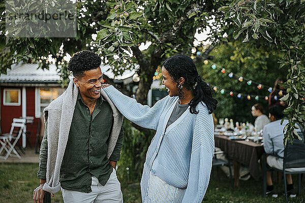 Happy young woman with hand on shoulder of male friend standing in back yard at dinner party