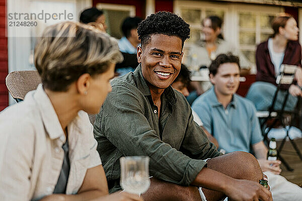 Portrait of smiling young man sitting with friend in back yard at social gathering