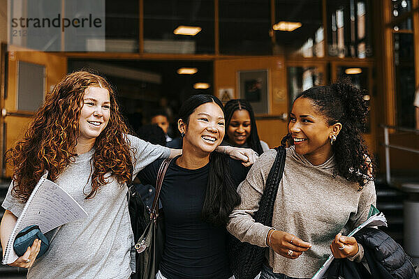 Happy multiracial female friends walking on school campus