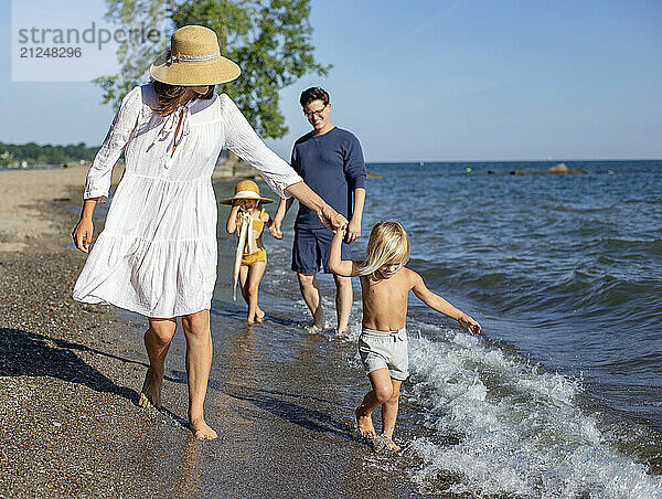 A family enjoys a sunny day at the beach  with a child playing in the waves and parents watching over.