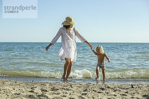 Mother and child  mother and son  holding hands on a sunny beach by the ocean.