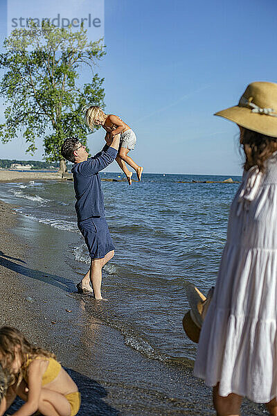 Father lifts up his young daughter on a sunny beach