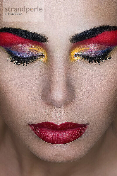 Close-up portrait of a woman with vibrant rainbow-colored eyeshadow and bold red lips.