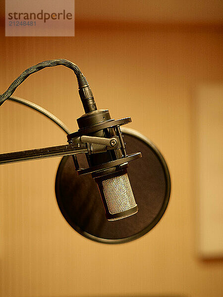 Condenser microphone with pop filter attached to a boom arm set against a blurred warm background.