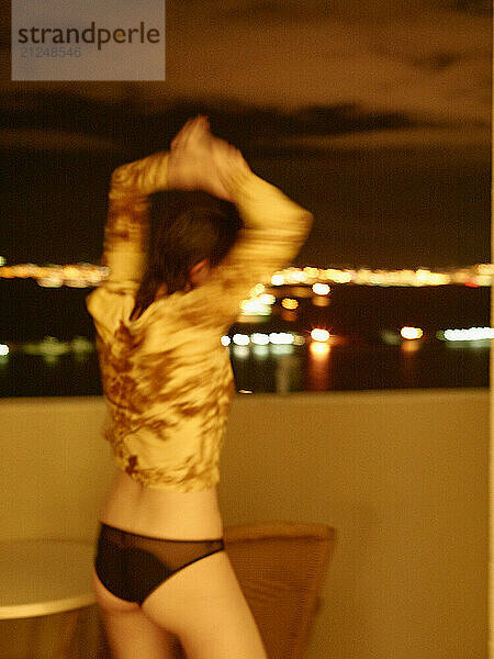 Woman standing on a balcony at night with city lights blurred in the background.