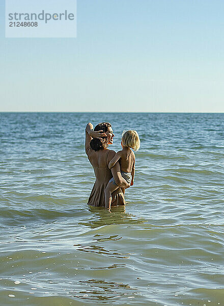 Mother and young child enjoying the sea together on a sunny day.