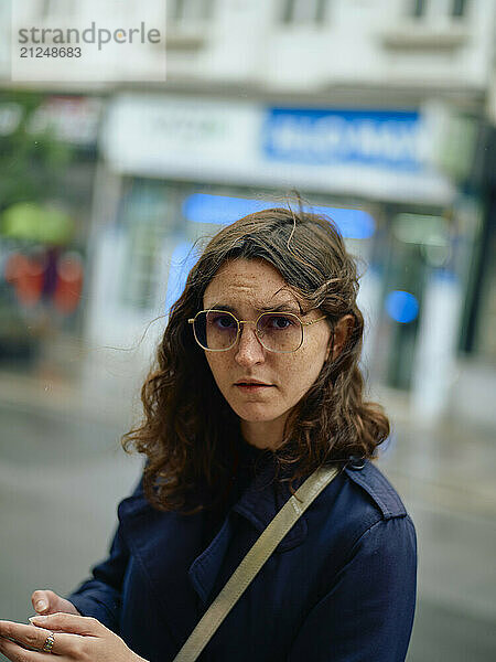 Woman with glasses looking pensively at the camera on a city street.