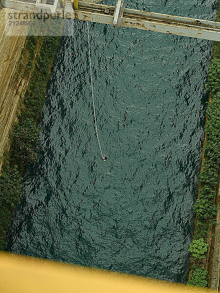 A person bungee jumping from a high bridge over a river surrounded by greenery.