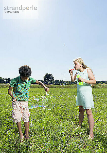 Boy and girl blowing bubbles together in a sunny green field.