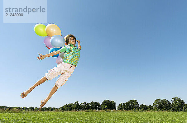 Boy flying with balloons outdoors on a sunny day.