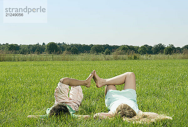 Boy and girl lying in a field in casual clothing during daytime.