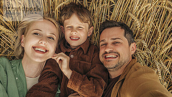 Father  son and mother lying on a wheat field  smiling and bonding  above view.