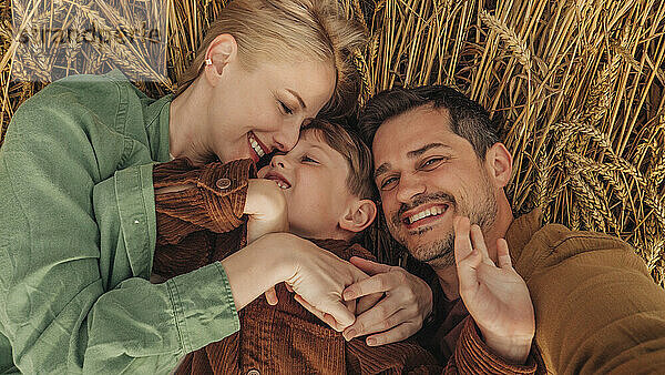 Father  son  and mother lying on wheat field  smiling and bonding outdoors in closeup above view.