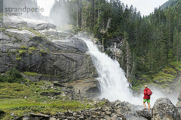 Hiker standing on rocks and looking at the Krimml Waterfalls in Hohe Tauern National Park  Salzburg Province  Austria.