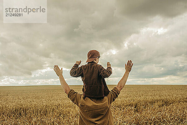 Father holding little son on shoulders in a wheat field  rear view.