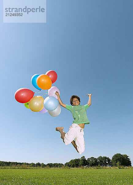 Boy jumping with balloons outdoors on a sunny day.