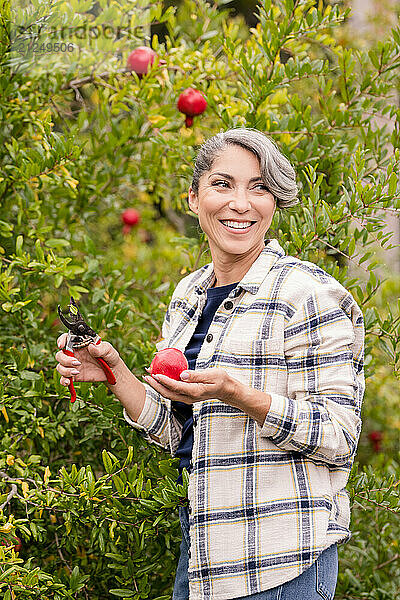 Woman smiling back while holding a pomegranate