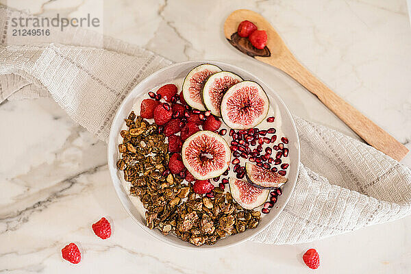 A bowl of yogurt with pomegranate seeds  figs  raspberries and granola