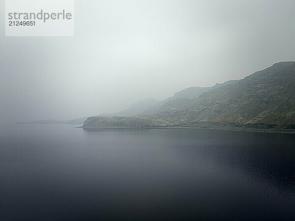 Calm seawater with fog next to hilly rocks