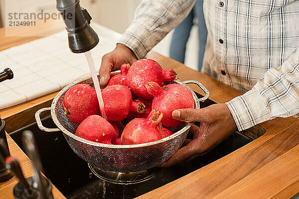 Man washing pomegranates in sink under running water