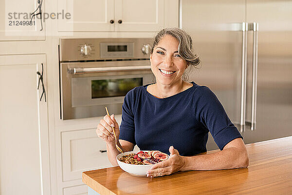 Woman smiling at camera with a bowl of yogurt in kitchen