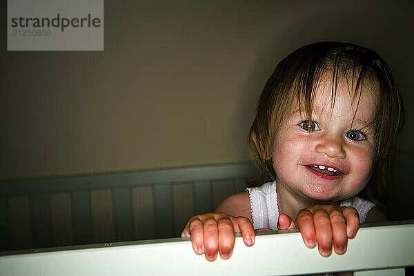 A 15-month-old girl is photographed smiling while standing in her crib