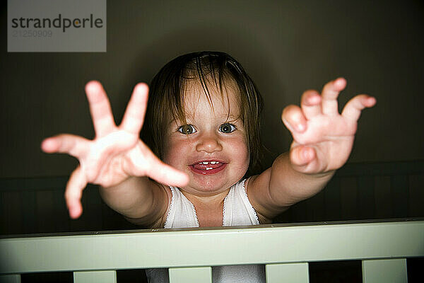 A 15-month-old girl is photographed smiling while standing in her crib