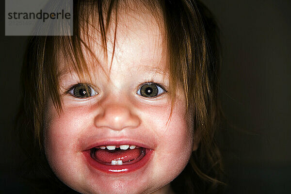 A 15-month-old girl is photographed smiling while standing in her crib