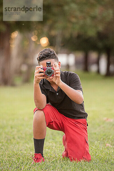 Young boy kneeling on the grass taking a picture with his camera