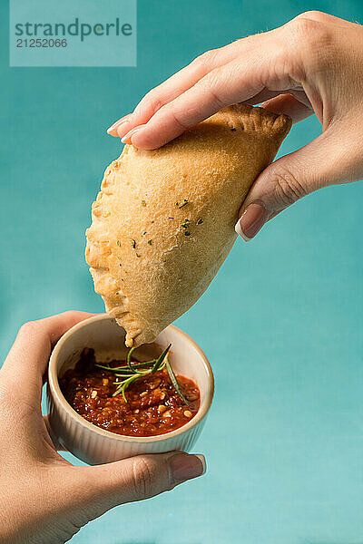 Hands dipping a meat pie in salsa