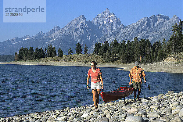 A couple carries a sea kayak on the shore of Jackson Lake in Grand Teton National Park  Jackson Hole  Wyoming.