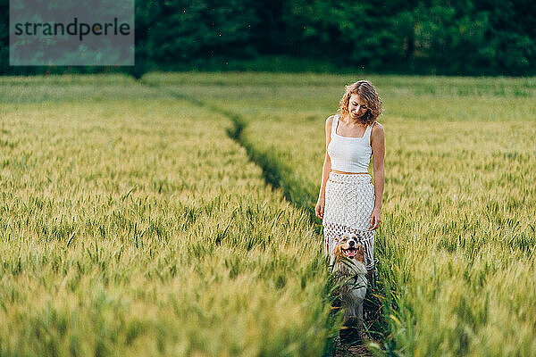 A young woman and her Australian Shepherd walk along a path in a field