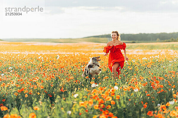 Young woman running with her dog in a poppy field on a sunny day