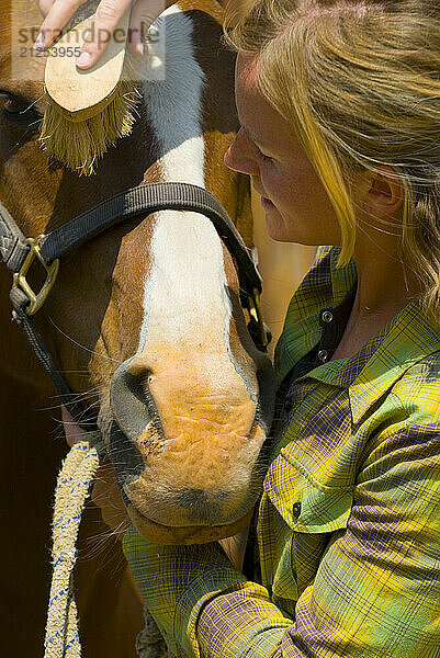 A young woman grooms her horse at a ranch in Wilson  Wyoming.