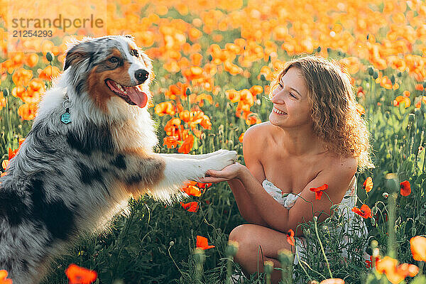 woman smiles she plays with her australian shepherd dog in poppy field