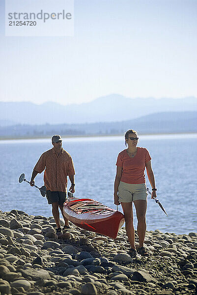 A couple carries a sea kayak on the shore of Jackson Lake in Grand Teton National Park  Jackson Hole  Wyoming.