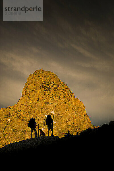 The Grand Teton looms behind two silhouetted hikers in the high alpine of the Teton Range  Wyoming.