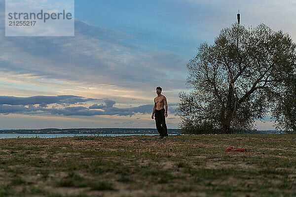 A man against the backdrop of the sunset sky on the shore of a lake.