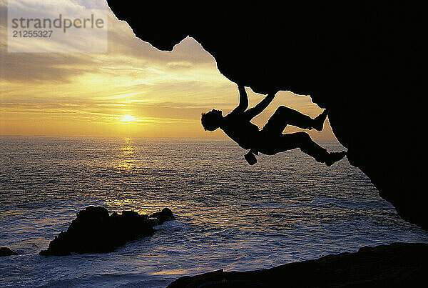 Kevin Jorgesen bouldering at sunset on the craggy Sonoma County coastline in Northern California. Bouldering is a kind of gymnastic rock climbing in which the climber uses his hands and feet to scale reasonalby small rocks without a rope or other equipment.