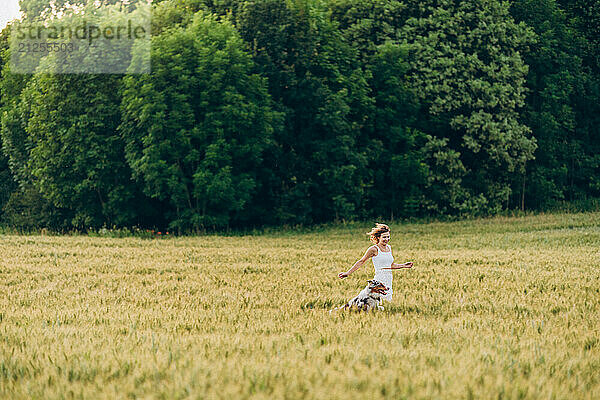 Young woman playing in green field with dog in summer