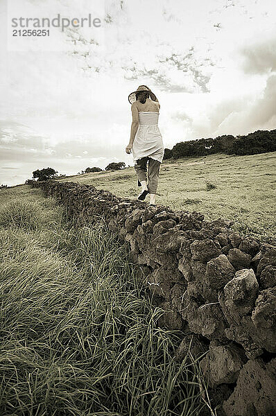 A young woman walks a stone fence along the Ulupalakua Ranch in upcountry Maui  Hawaii.