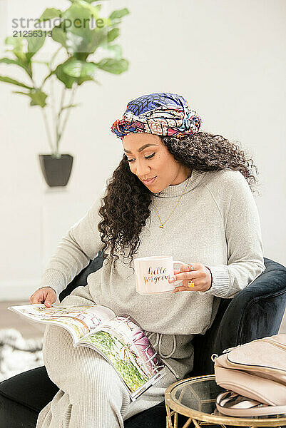 Woman with curly hair looking at a magazine and holding a mug