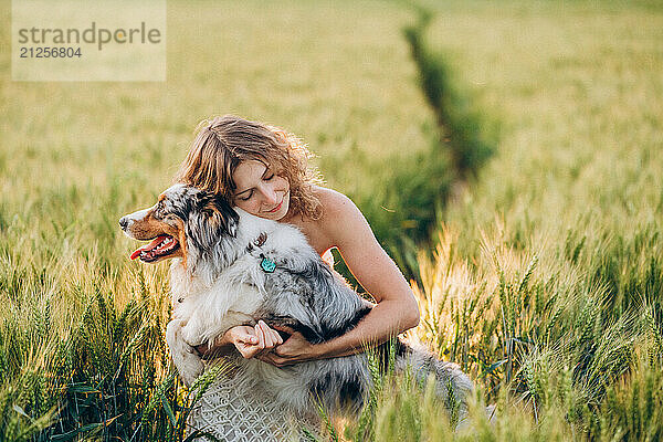 woman with her australian shepherd in a green rye field