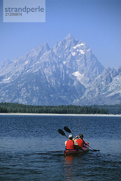 A young couple paddles a tandem sea kayak across Jackson Lake on a sunny day in Grand Teton National Park  Jackson Hole  Wyoming.