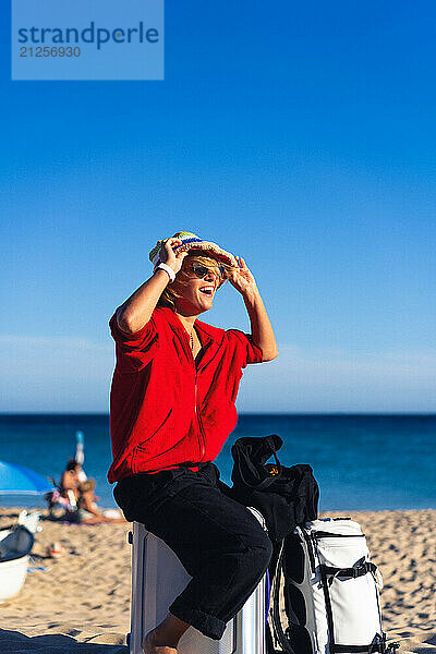 A woman travels  sits on a suitcase on the beach.